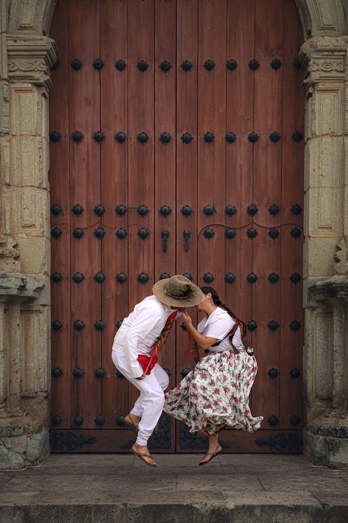 A couple performing a traditional dance in cultural attire in front of a historic wooden door.